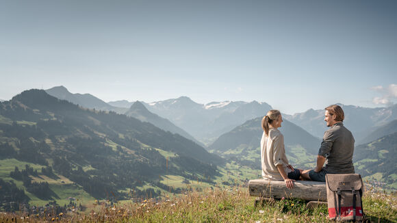 Ein auf einem Bänkchen auf dem Rellerli sitzendes Pärchen das die Aussicht auf die schöne Bergwelt oberhalb Gstaad geniesst.